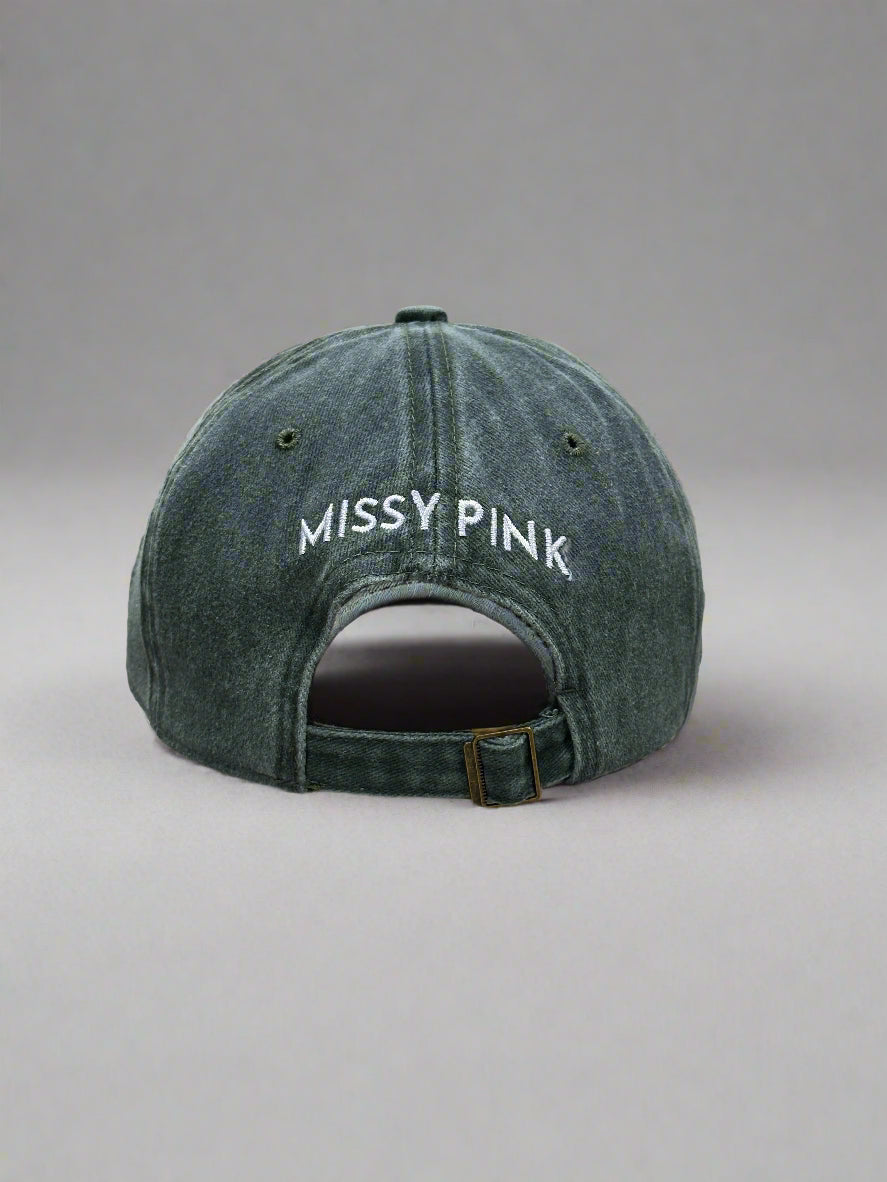 Gray cap with 'MISSY PINK' text on a clear stand against a blurred background